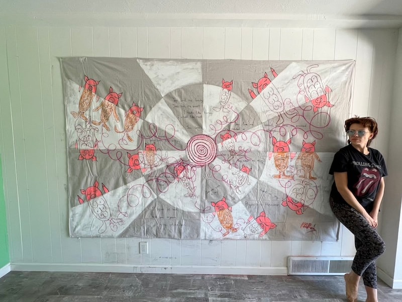 Marina Orlova posing beside large fabric installation with red line drawings of animals and spirals